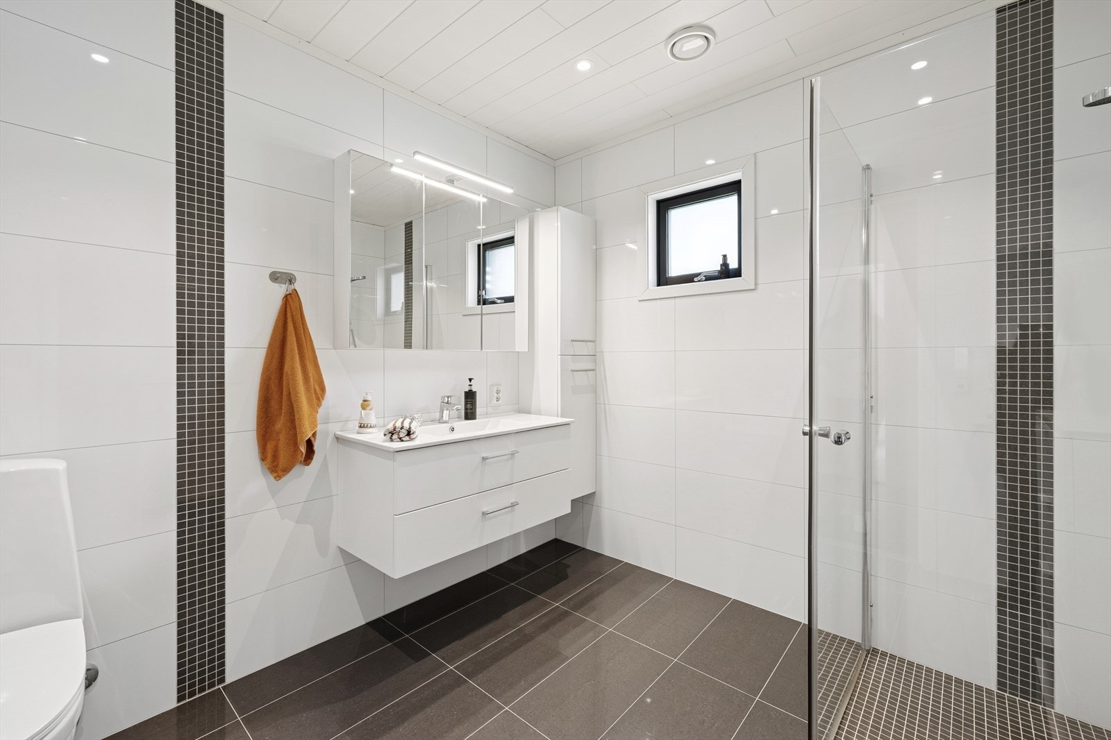Flott bad med fliser på vegger og gulv med gulvvarme. Badet har innredning med servant, overskap med speil og tilhørende belysning, toalett og dusjhjørne. Galleribilde