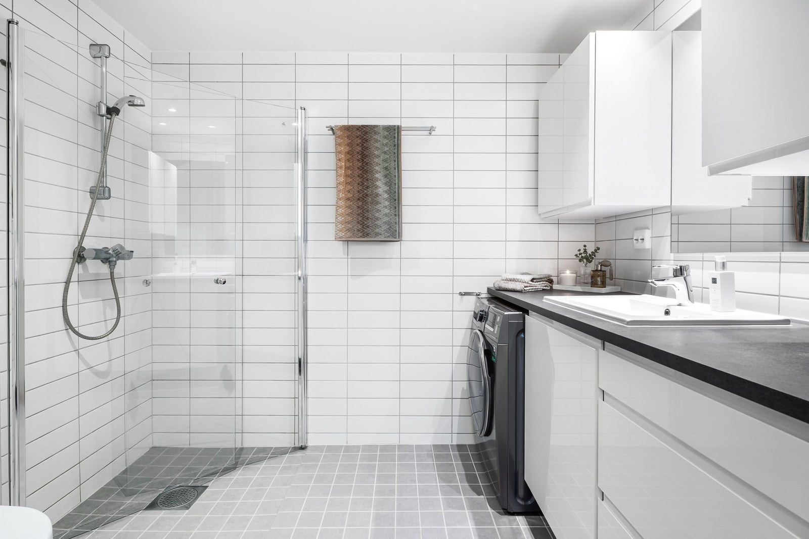 Opplegg for vaskemaskin, veggmontert toalett, dusjdører i herdet glass, baderomsinnredning med høyglans fronter og laminat benkeplate med nedfelt servant Galleribilde