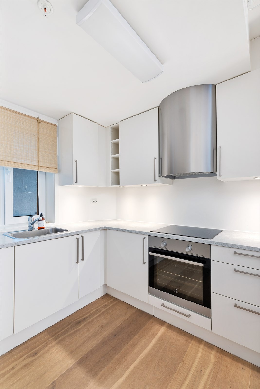 Kjøkken fra HTH med integrerte hvitevarer bestående av koketopp, stekovn, oppvaskmaskin og kjøleskap. Benkeplate i laminat med helsparklet og malte vegger mellom Galleribilde