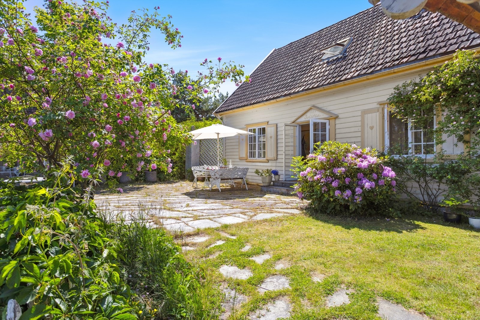 På terrassen nyter du både sol og utsikt i harmoniske omgivelser, omringet av rosebusker og idyllisk beplantning. Galleribilde