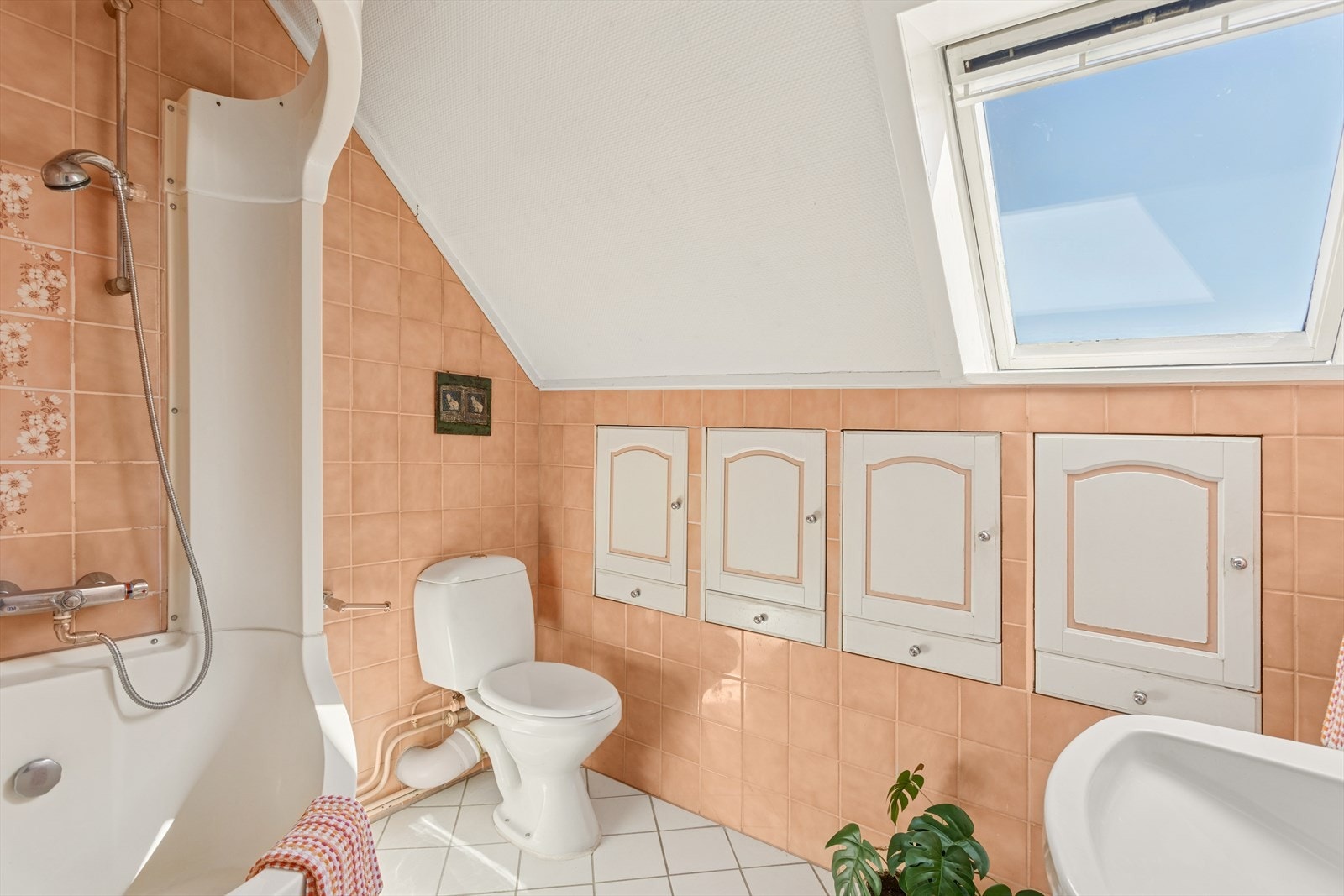 Badet i andre etasje er fra 1980-tallet, og har retro flislagte vegger i en søt ferskenfarge, hvitt flislagt gulv, servant, toalett og badekar med dusj. Galleribilde