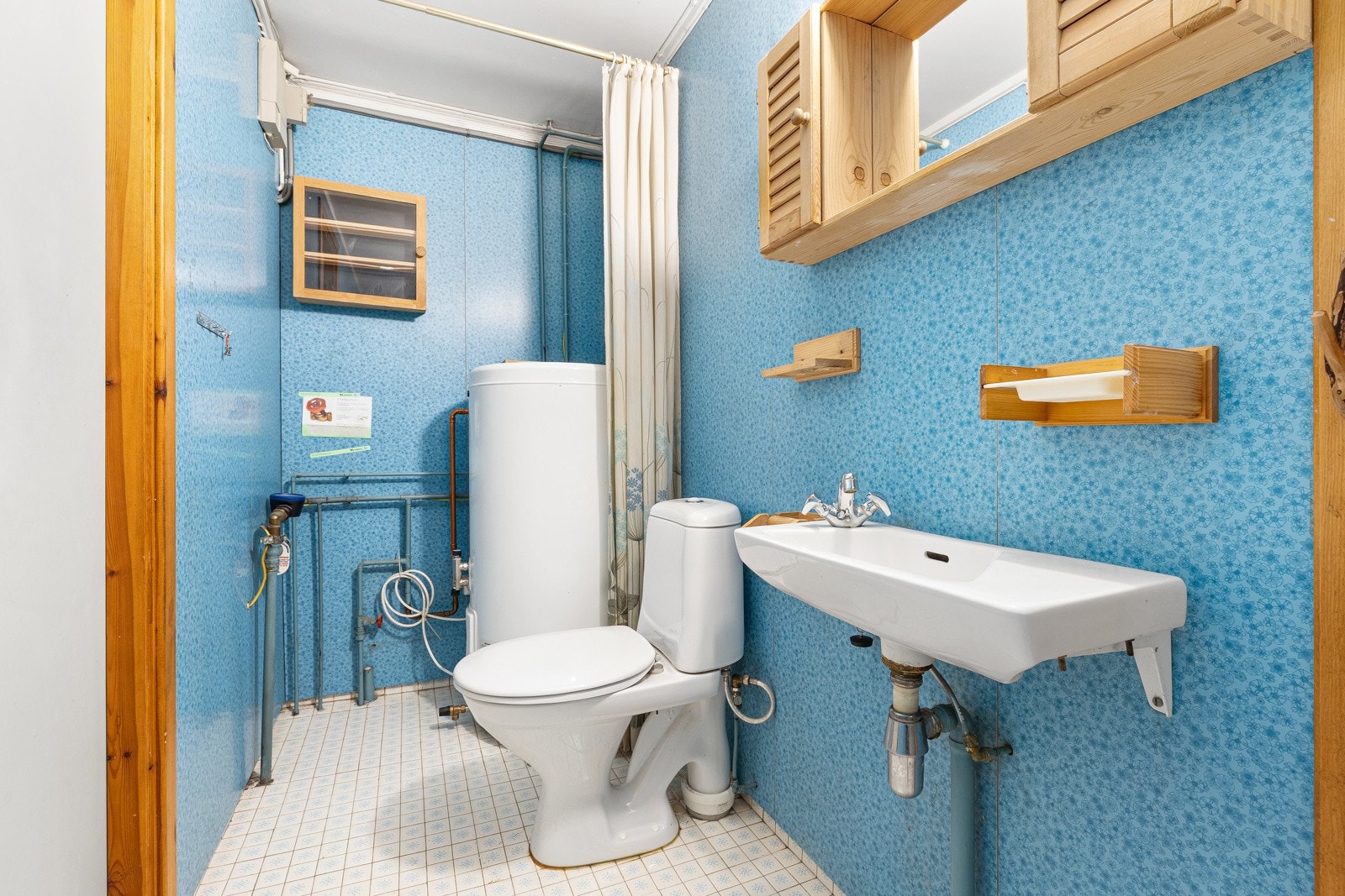 Baderom fra byggeår. Flislagt gulv med gulvvarme. Veggflater belagt med våtromsplater. Himling i lysmalt slett flate. Vegghengt servant med to-greps armatur. Galleribilde