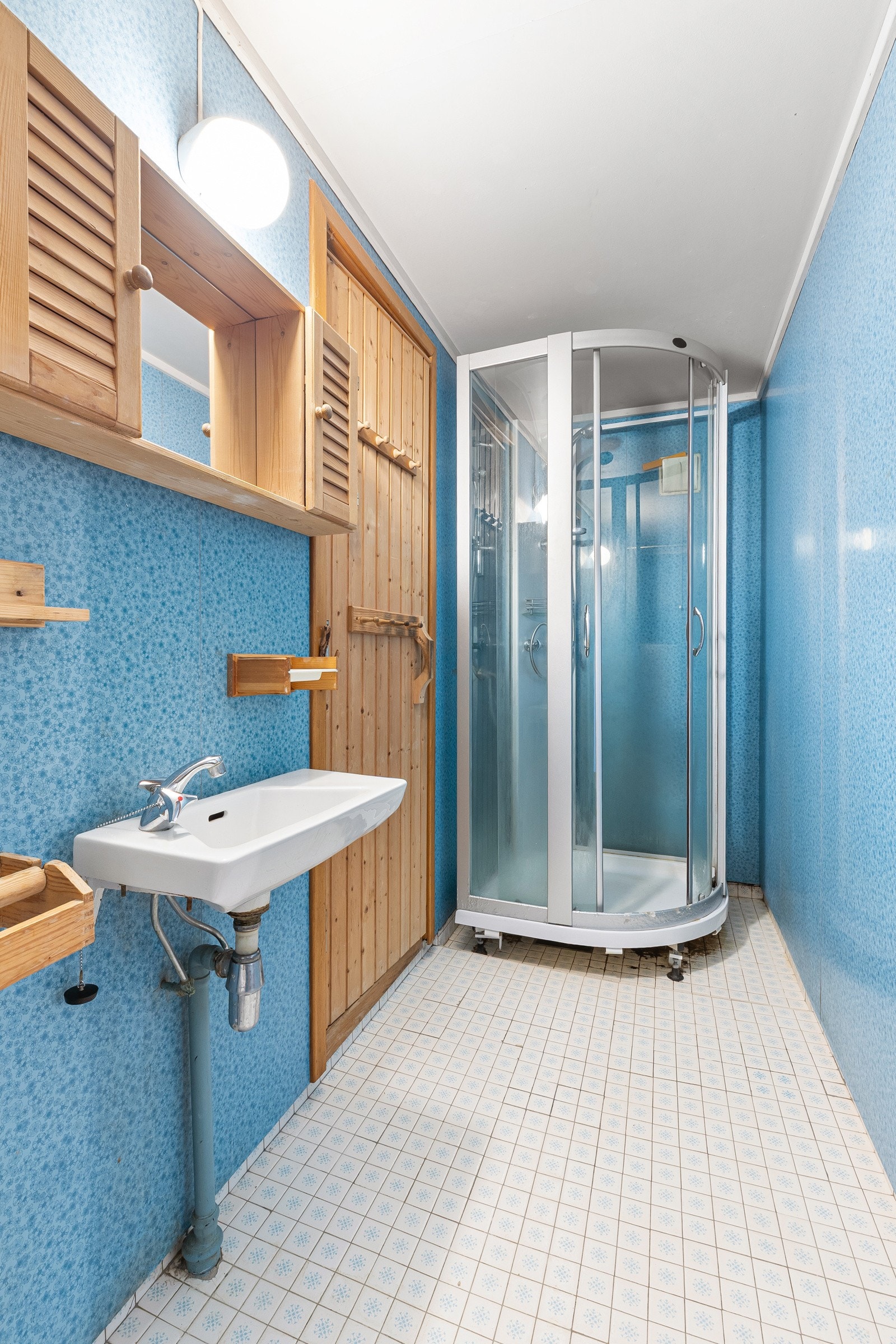 Baderom fra byggeår. Flislagt gulv med gulvvarme. Veggflater belagt med våtromsplater. Himling i lysmalt slett flate. Vegghengt servant med to-greps armatur. Galleribilde