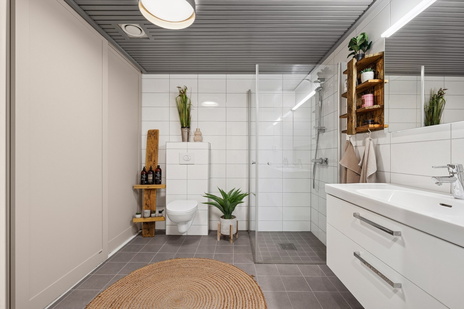 Bad/wc/vaskerom med fliser på gulv og vegger. Bak skyvedørene er alt av vaskeromsartikler diskret plassert. Galleribilde