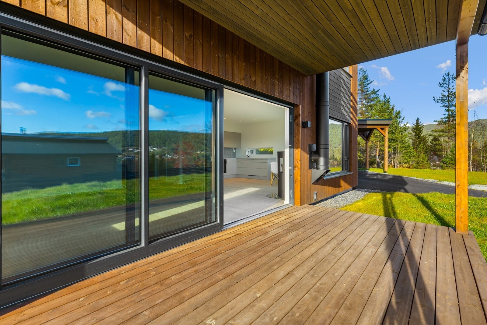 Boligen har store vinduflater og stor skyvedør som leder ut mot overbygget terrasse og hage. Galleribilde