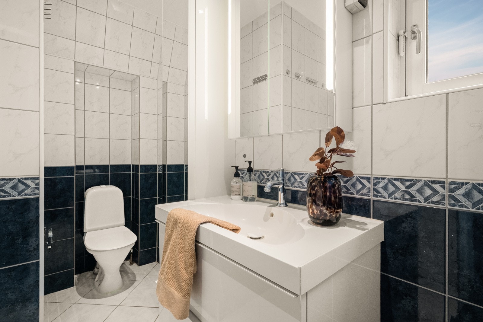 Badet er heldekkende med flislagt gulv og vegger, og utstyrt med toalett, heldekkende servant og belyst speil. Galleribilde