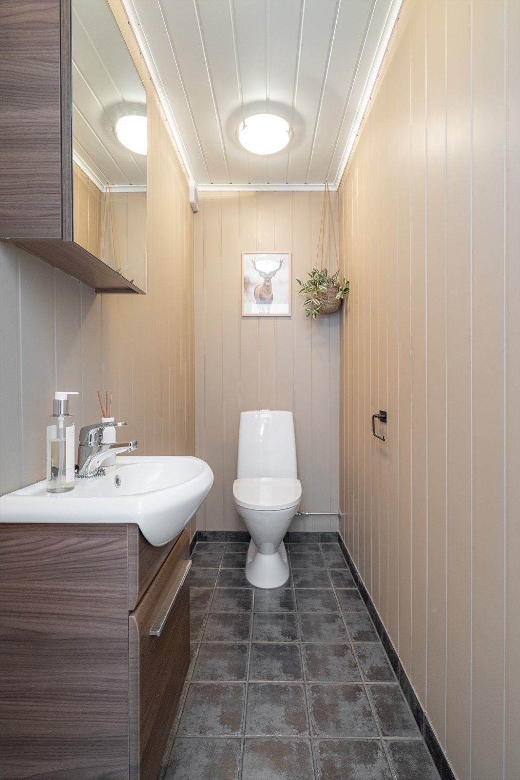 Inntil badet er det eget toalettrom, med flislagt gulv og MDF-plater på veggene som er malt i 2020. Toalettet har en moderne innredning med servantskap og speilskap. Galleribilde