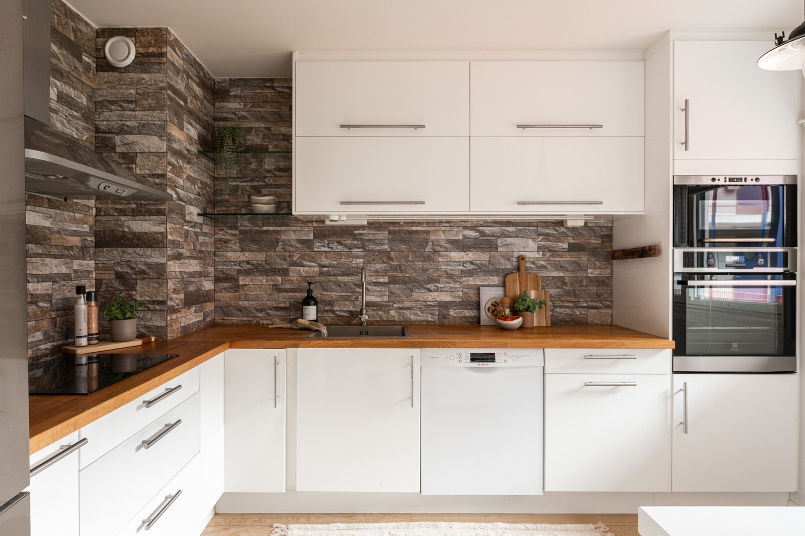 Separat og tidløst kjøkken med benkeplater i eik, platetopp, hetteventilator og steinfliser over benk. Galleribilde