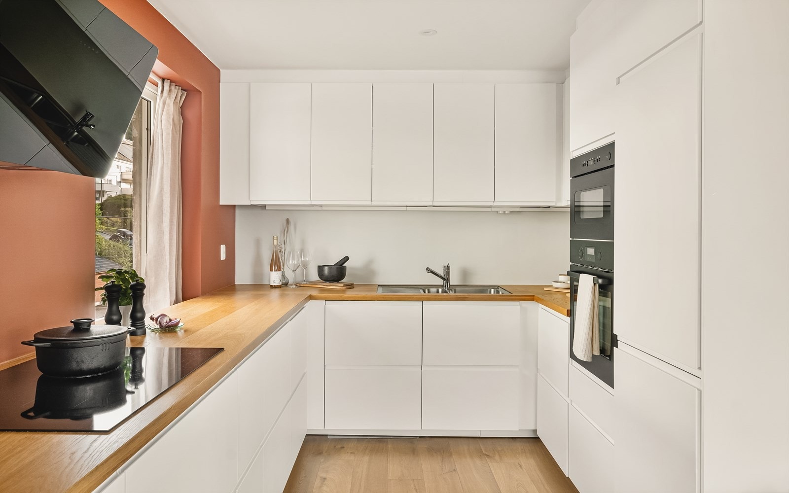 Moderne IKEA-innredning med slette, hvite fronter og benkeplate med finért toppsjikt. Stål vaskekum, ventilator og integrerte hvitevarer fra IKEA: stekeovn, induksjonstopp (78 cm), oppvaskmaskin, mikrobølgeovn og kombiskap. Galleribilde