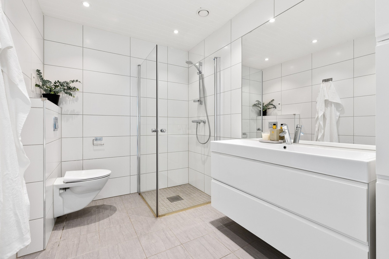 Badet har et pent uttrykk med hvite vegg- og gulvfliser, innfelt downlights og varmekabler. Galleribilde