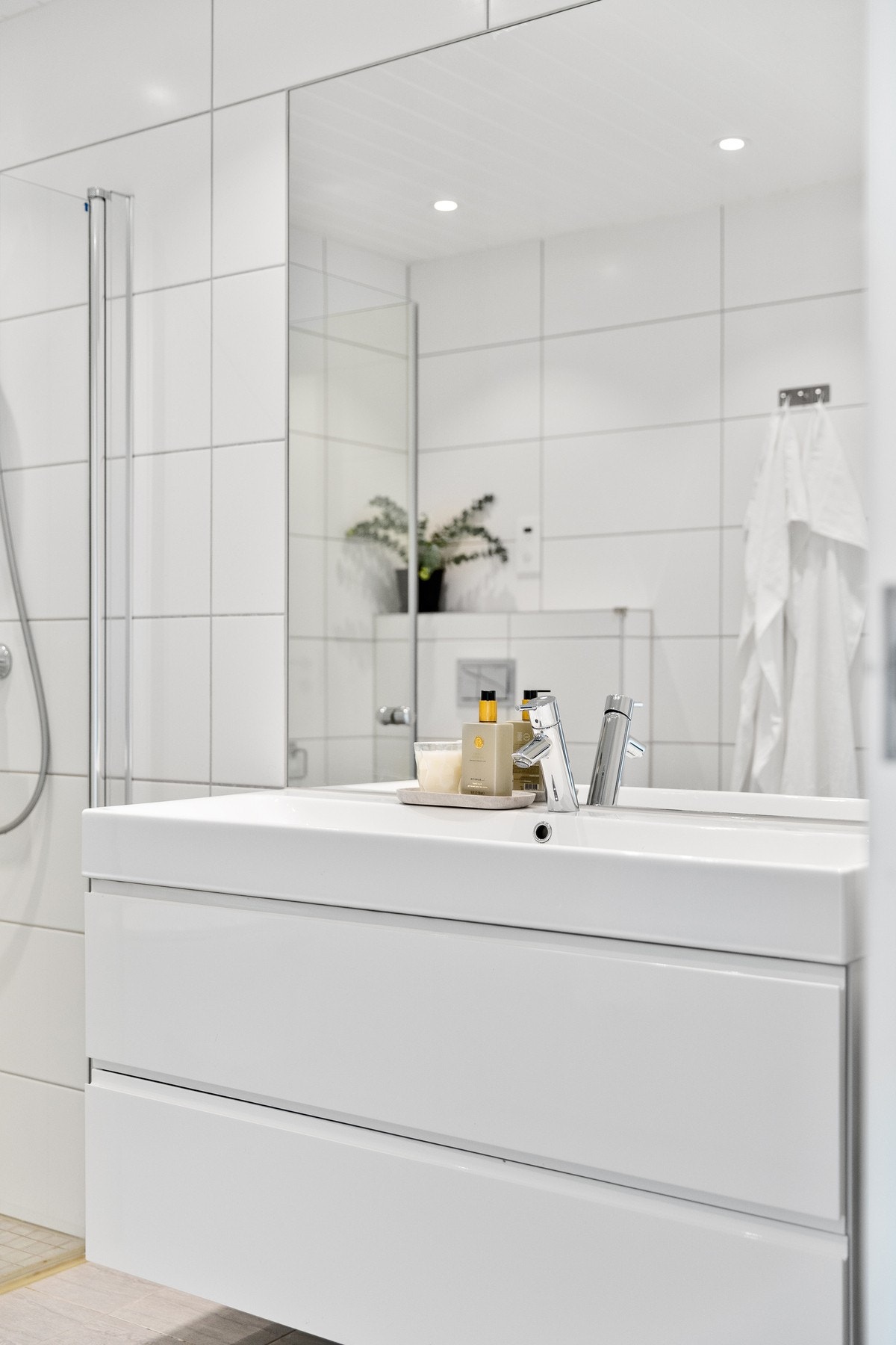 Innredet med servantinnredning, innmurt speil på vegg over servant, ett høyskap, vegghengt toalett og dusjhjørne med svingbare glassdører. Galleribilde