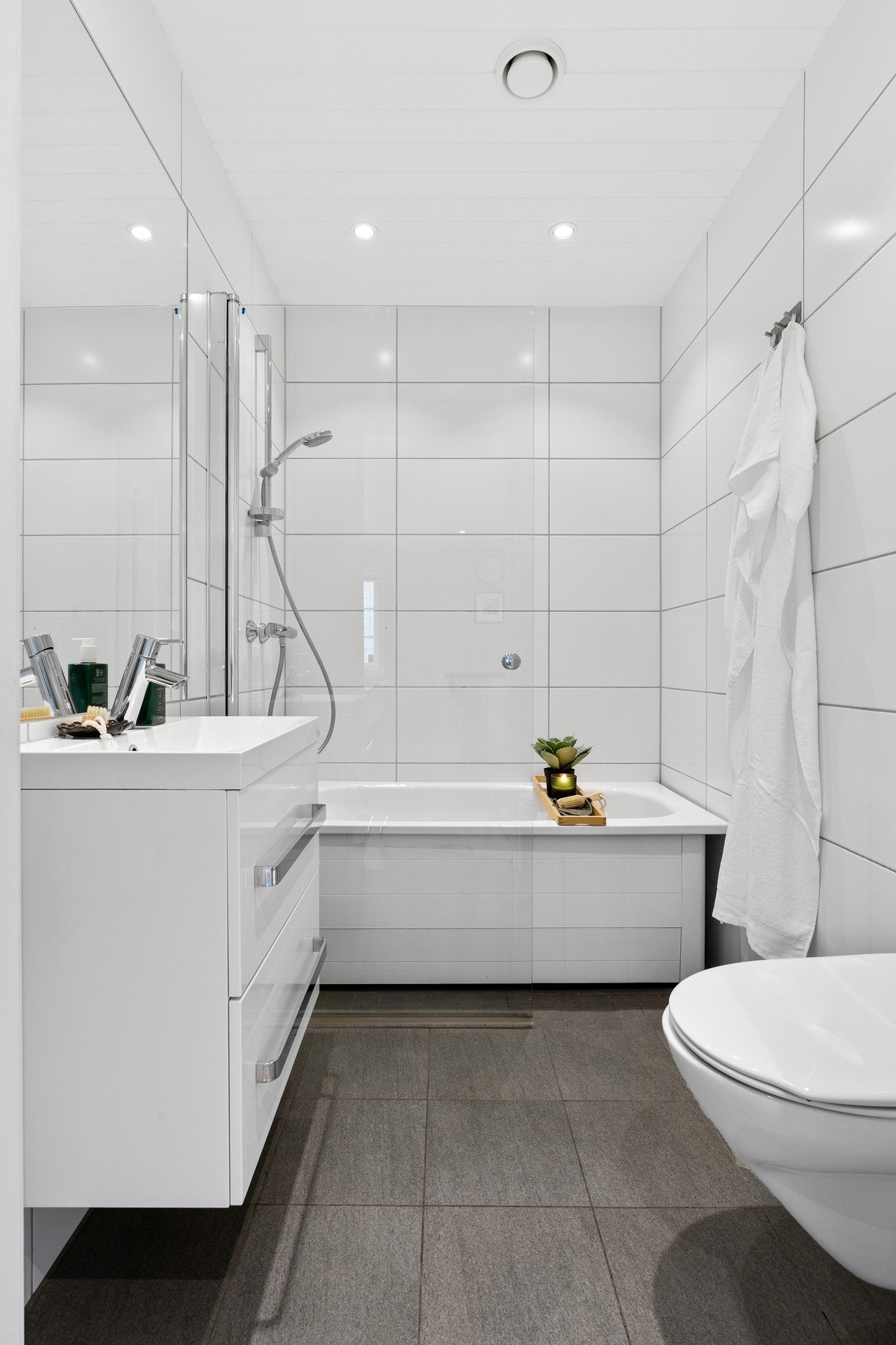 Badet har et pent uttrykk med hvite vegg- og gulvfliser, innfelt downlights og varmekabler. Galleribilde