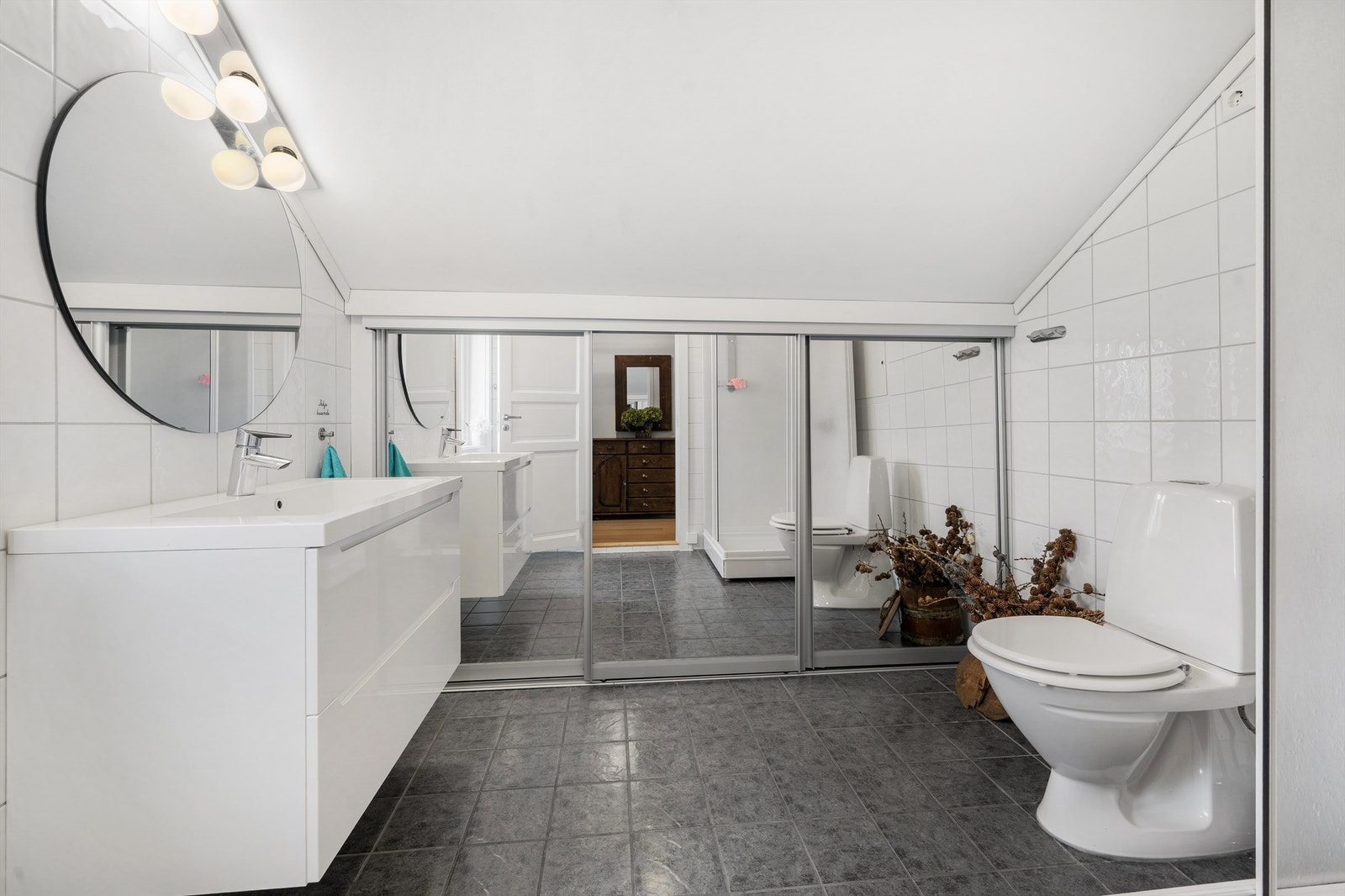 Flislagt bad med innredning med god oppbevaringsplass og praktisk skyvedørsgarderobe Galleribilde