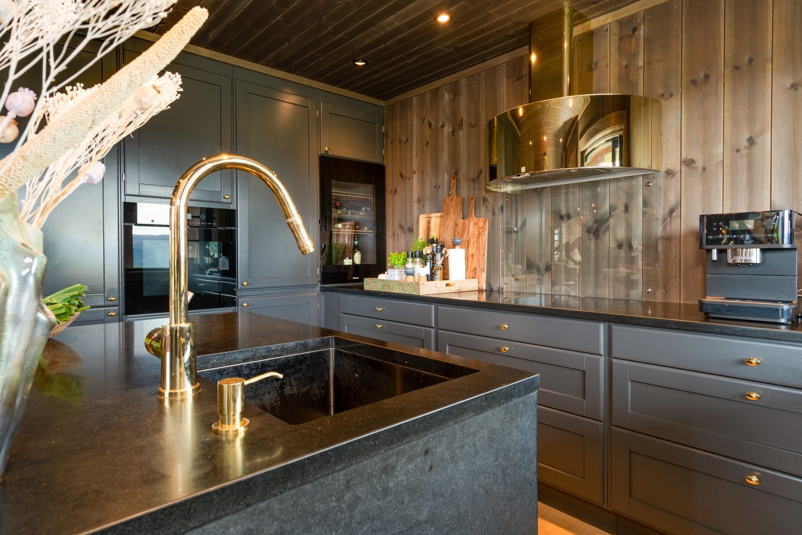 Kjøkkenet har en spesialtilpasset innredning og hvitevarene er fra kvalitetsleverandøren Miele. Over kokesonen henger en lekker messingfarget ventilator fra Røroshetta, som står i stil med kjøkkenarmaturet og håndtakene på skap og skuffer.