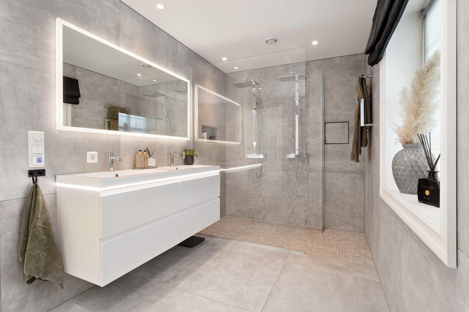 Badet i 1. etasje er lekkert innredet og har et innbydende design. Det er utstyrt med innredning med dobbelservant, speil med integrert belysning, dusj med glassvegg og dør, samt to dusjarmaturer og et vegghengt toalett. Galleribilde