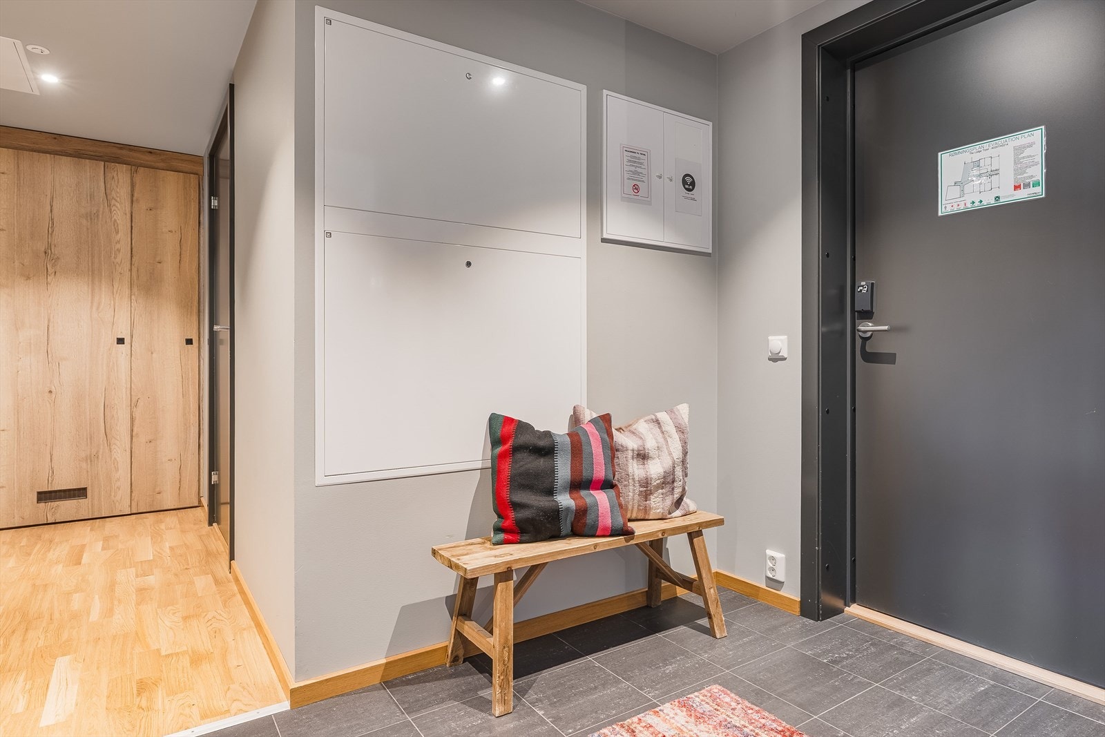 Entréen har grå fliser på gulv med gulvvarme, glatte malte overflater, skjult elektrisk anlegg og downlights i himlingen. Galleribilde