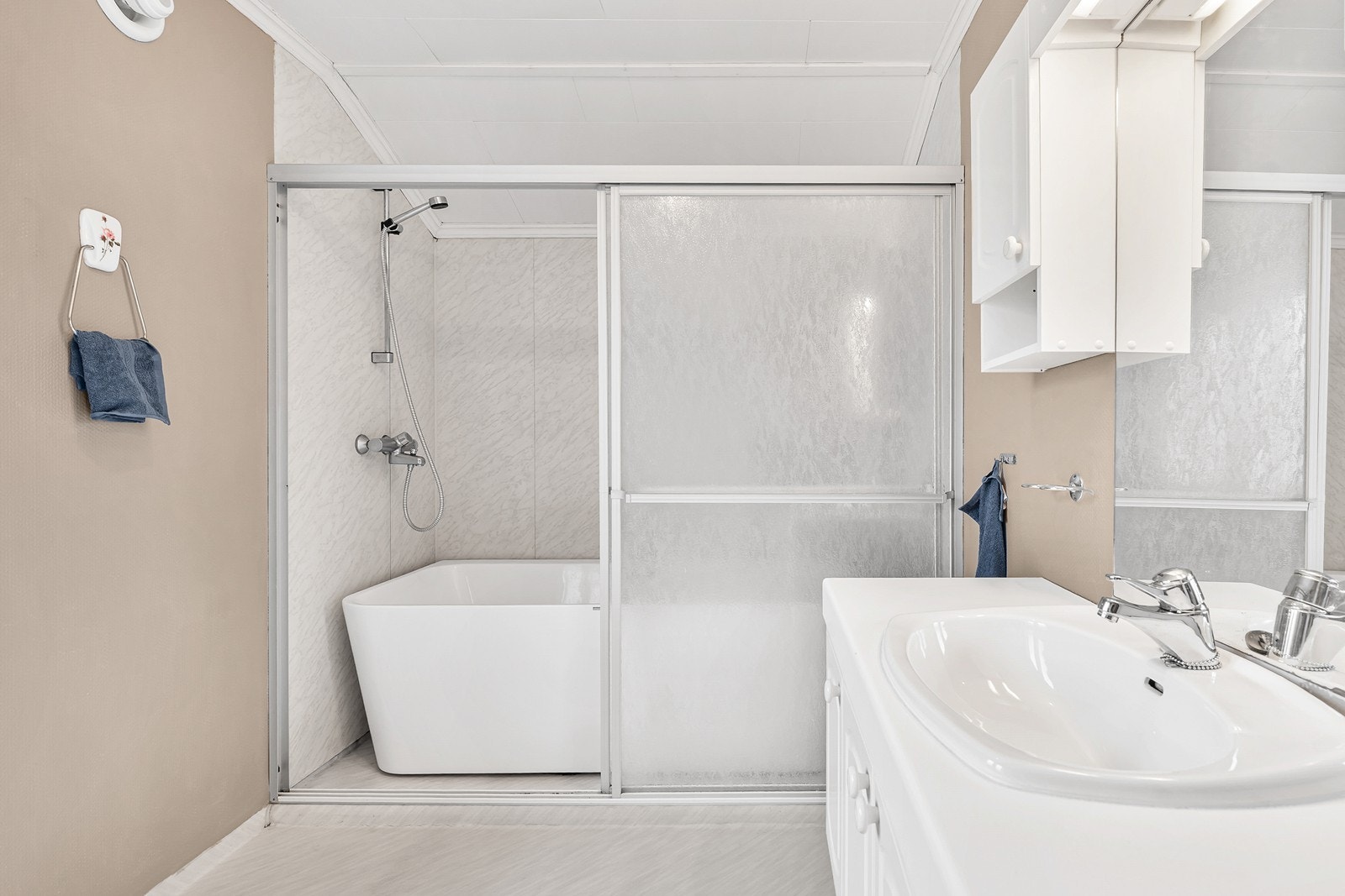 Badet har gulvbelegg med varmekabler, baderomsplater i dusjsone og er innredet med toalett, servant og badekar med dusjløsning Galleribilde