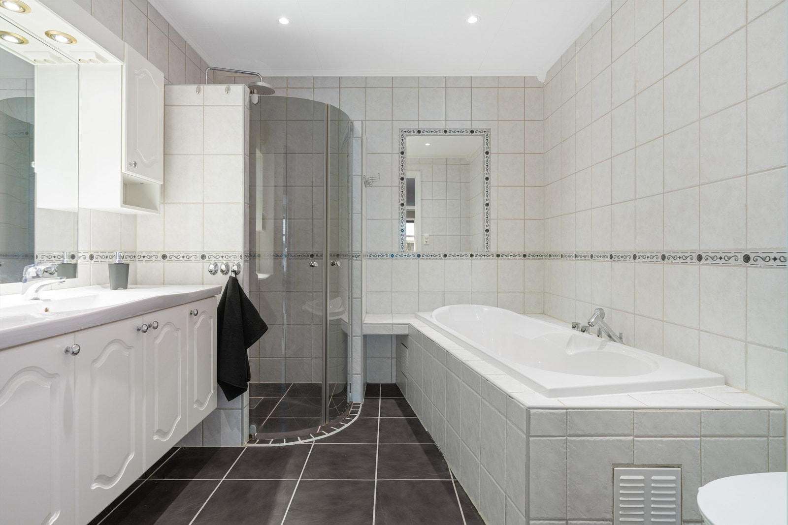 Pent flislagt bad på 6,5 kvm med gulvvarme og downlights i himling. Videre er badet utstyrt med servantskap med overskap og speil med lys, vegghengt toalett, dusjhjørne og badekar. Galleribilde