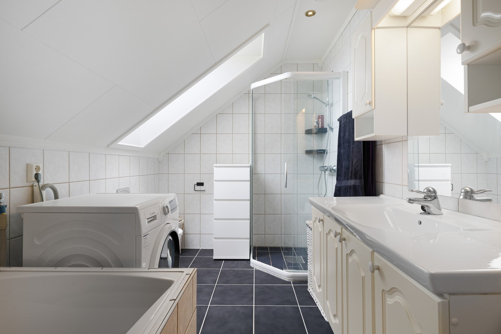 Pent flislagt bad på 6 kvm med gulvvarme, downlights og opplegg for vaskemaskin. Videre er badet utstyrt med servantskap med overskap og speil med lys, vegghengt toalett, dusjhjørne og badekar. Galleribilde