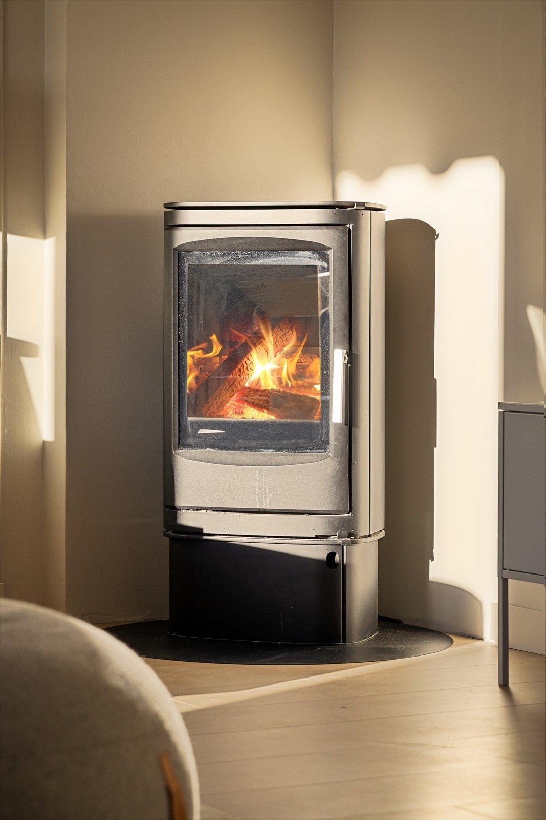 Koselig peisovn med glassdør på ildfast plate, omgitt av pusset teglsteinspipe. Galleribilde