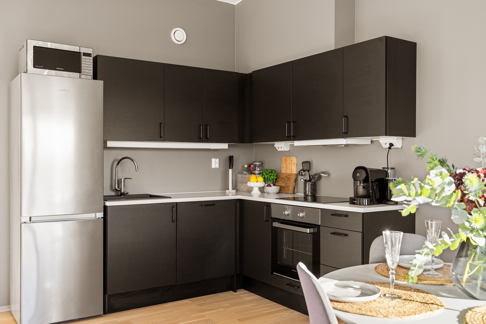 Kjøkkenet har matte, mørke fronter og lyse benkeflater i en L-form som gir effektiv arbeidsflyt. Galleribilde