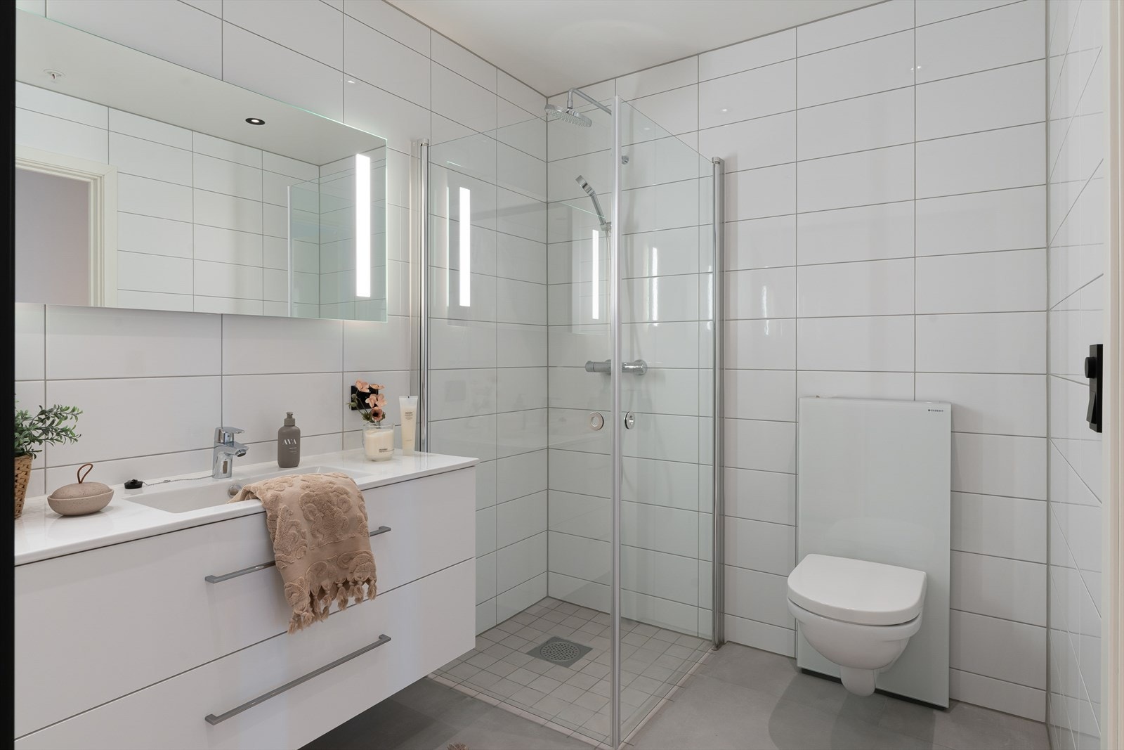 Flott helfliset bad med vegghengt wc, dusjhjørne og varme i gulv for ekstra komfort. Badet fremstår som arealeffektivt med pen baderomsinnredning i hvit utførelse. Galleribilde