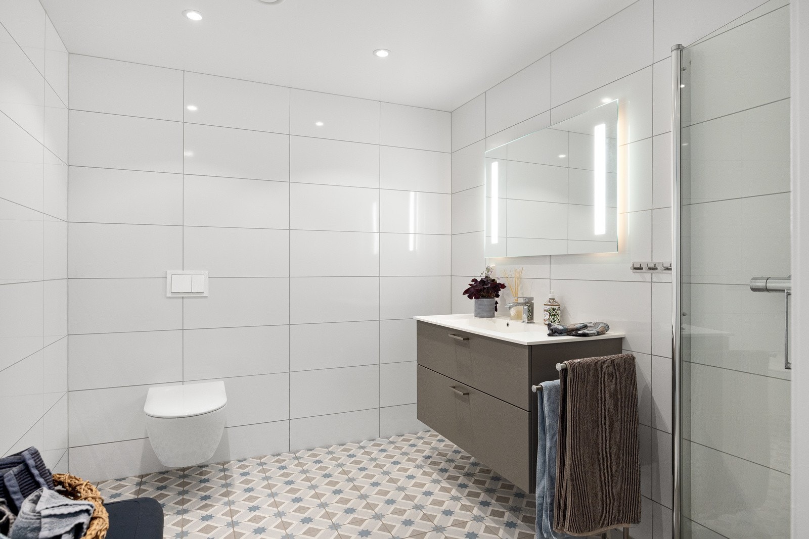 Hovedbadet er romslig og innbydende, med delikate fliser, svingbare glassdører i dusjsonen, vegghengt toalett og enkel servant med underskap Galleribilde