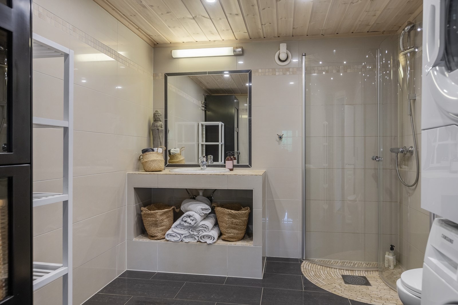 Bad/vaskerom har fliser på gulv og vegg, samt vannbåren gulvvarme og og varmekabler. Innredet med nedfelt servant, veggmontert toalett, dusjhjørne og opplegg til vaskemaskin. Galleribilde