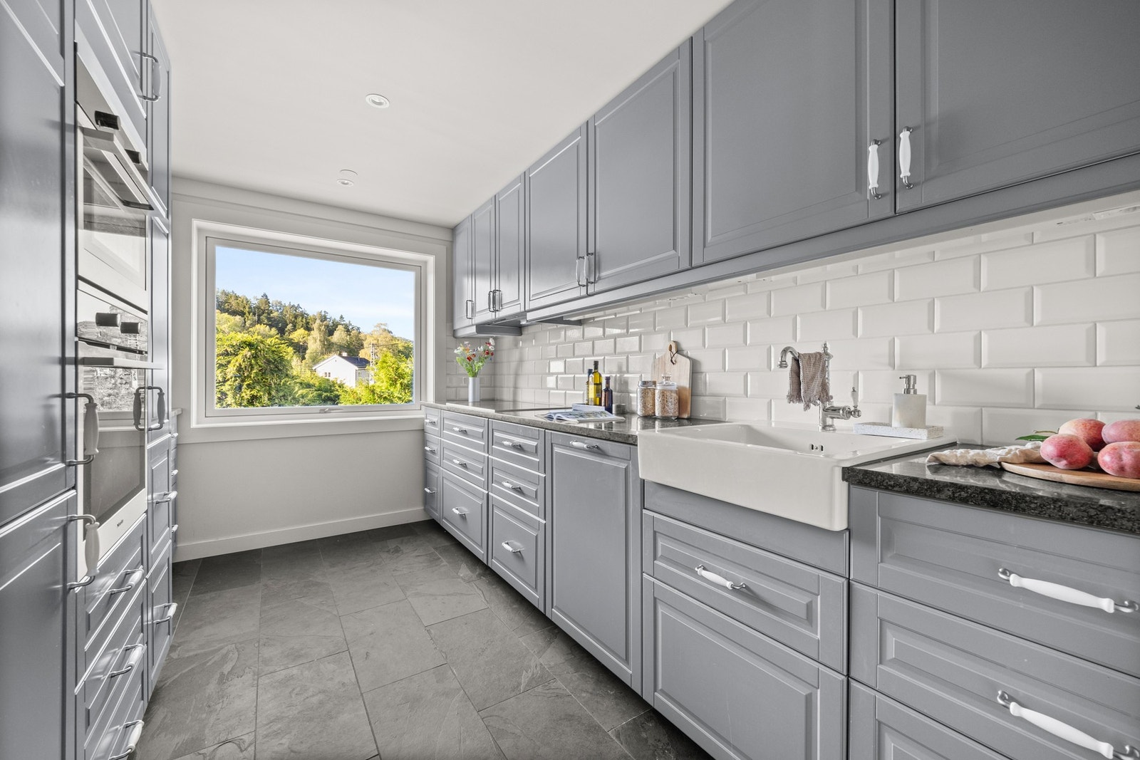 Kjøkkenet er utformet med gode materialvalg. Med profilerte fronter, stein benkeplate, og ovenpåliggende oppvaskkum, er det både stilfullt og funksjonelt. Galleribilde