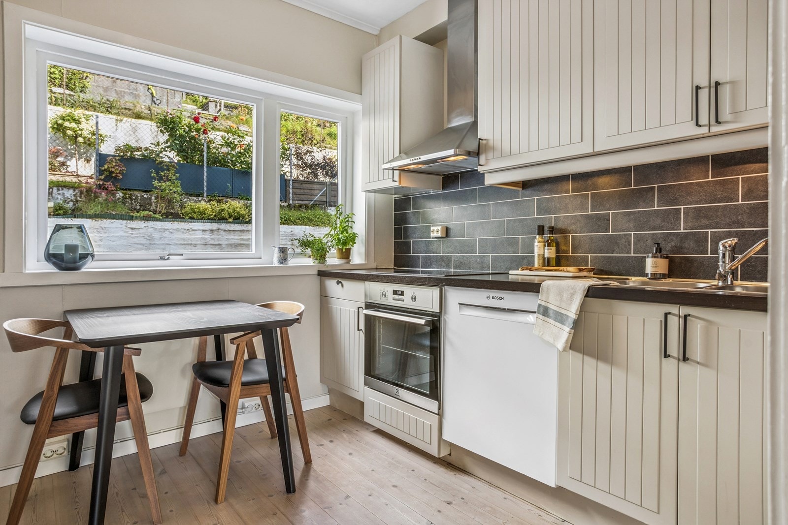 Pent kjøkken med innredning fra Ikea. Kjøkkenet har profilerte fronter, benkeplater av laminat og fliser over benk. Vegger og fronter er malt, og det er nye håndtak på frontene Galleribilde