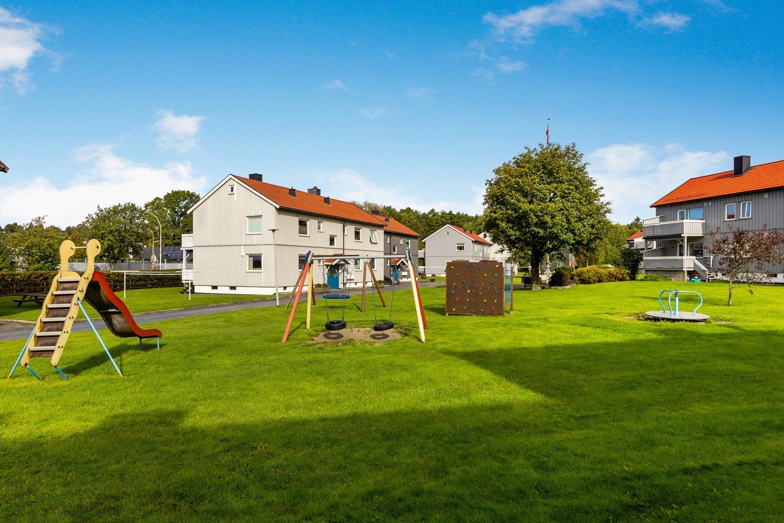 Pent opparbeidete fellesarealer med gressplen, asfalterte gangarealer, lekeapparater for barna, og sittebenker Galleribilde