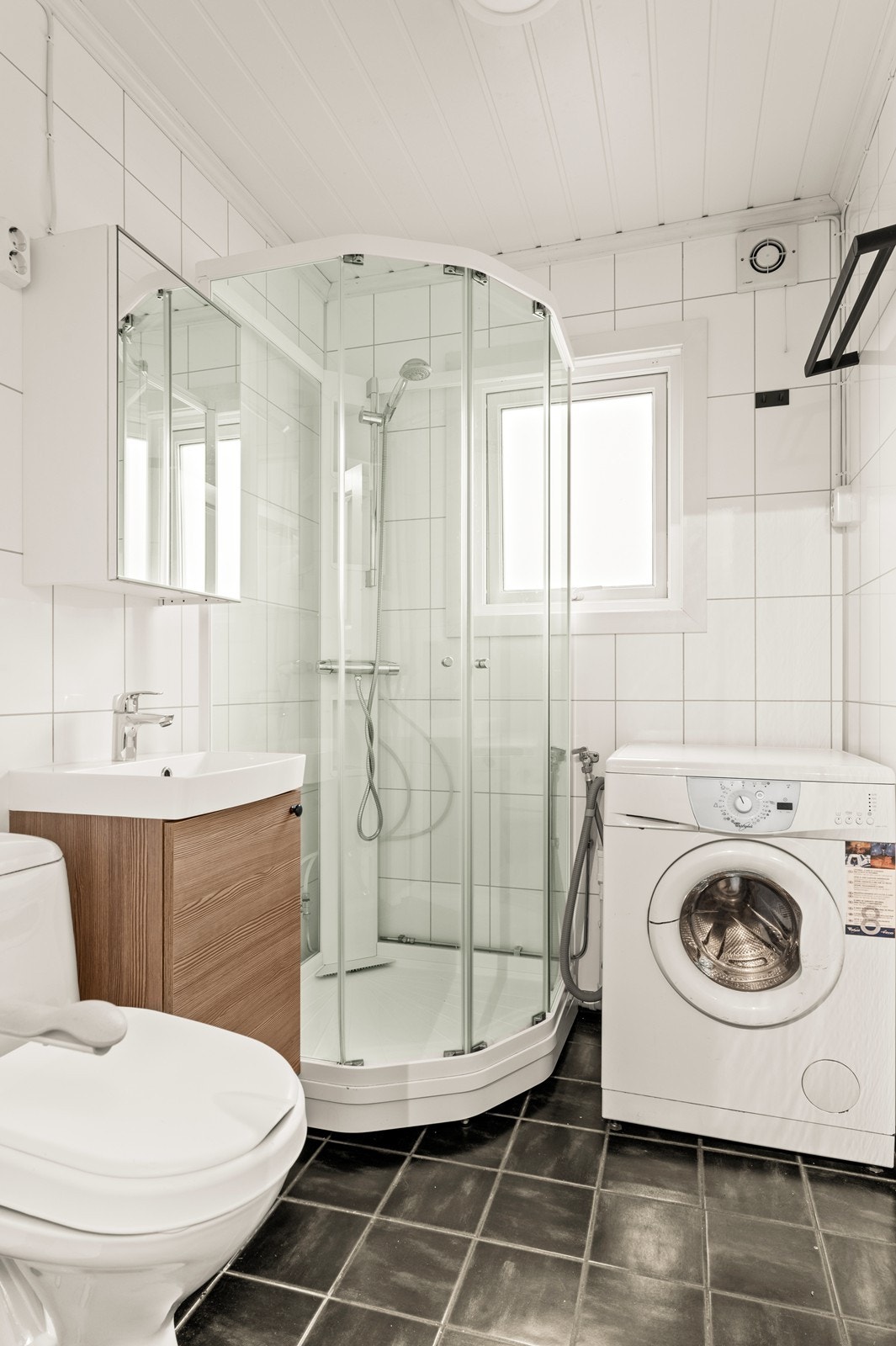 Baderommet har fliser på gulvet med med elektriske varmekabler. På veggene er det våtromsplater. Det er innredet med servantskap med heldekkende servant, overskap med speil, dusjkabinett, wc og opplegg for vaskemaskin Galleribilde