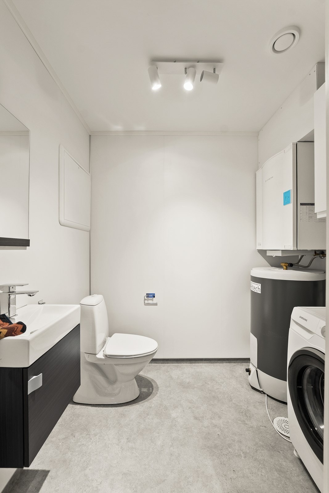 Moderne vaskerom/toalettrom med gulvvarme, servant, toalett, speil, ventilasjonsvifte, varmtvannsbereder og opplegg til vaskemaskin. Galleribilde