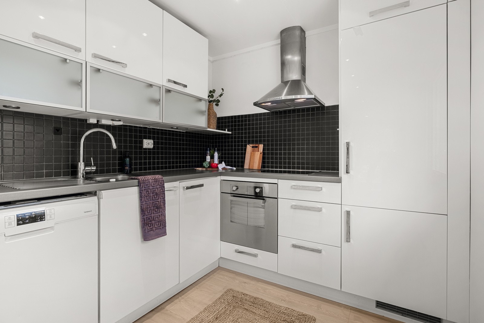 Mellom benk og overskap er det lagt sorte fliser, som gir et stilrent uttrykk og samtidig er praktisk i bruk. Under overskapene er det montert lys som gir god arbeidsbelysning. Galleribilde