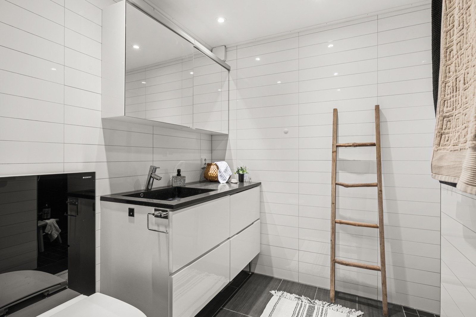 Badet er utstyrt med servant integrert i steinplate med ettgreps blandebatteri, skuffer under og speilskap med belysning over. Videre finner du vegghengt toalett med glassisterne utenpå vegg, samt opplegg for vaskemaskin. Galleribilde