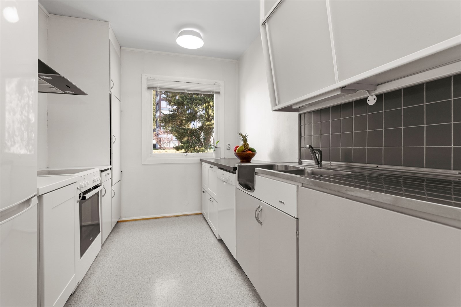 Kjøkkenet har en praktisk innredning med plassbygde overskap og høyskap i lys, glatt utførelse, kombinert med hvite, profilerte høyskap og underskap som gir et tidløst uttrykk. Galleribilde