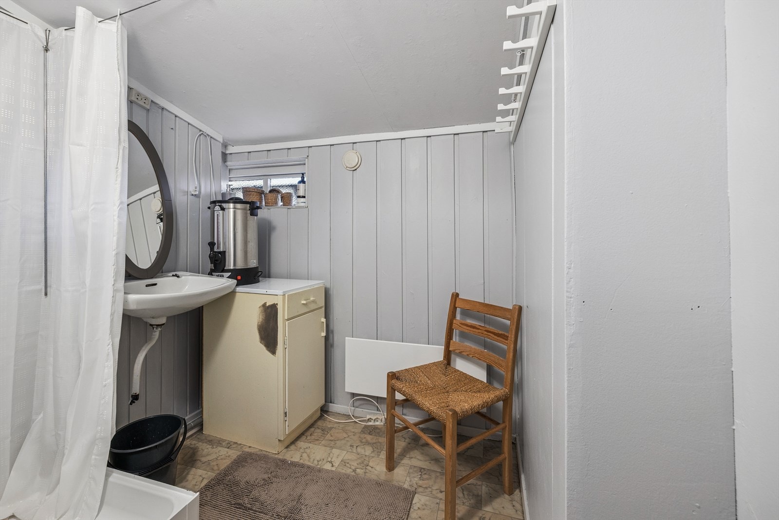 Sanitærrom med belegg på gulv og mat panel på vegger. Rommet er utstyrt med servant, dusj med forheng og egen pumpe. Galleribilde