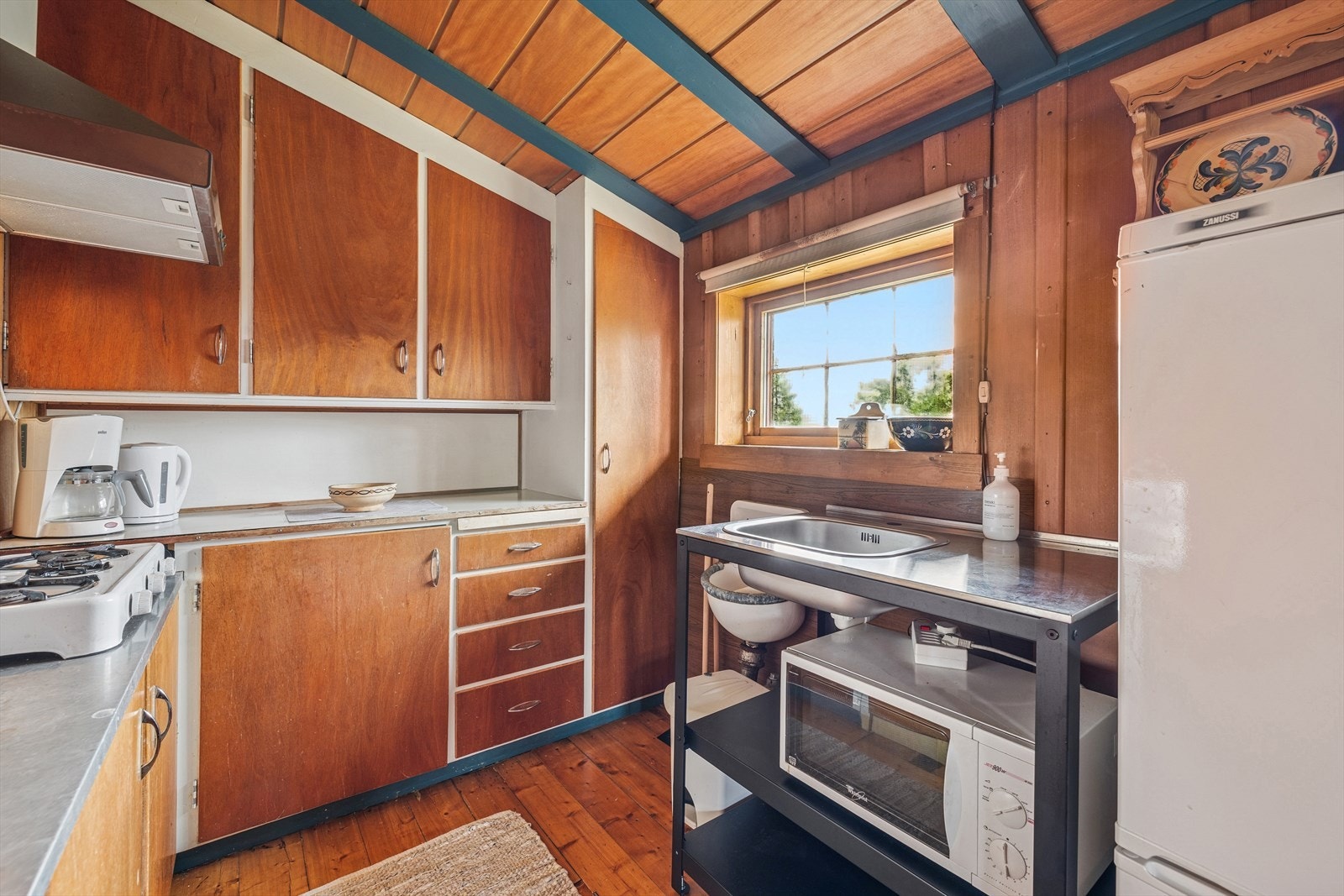 Kjøkkeninnredning med laminerte skrog, glatte fronter og laminert benkeplate. Kjøkkenet er utstyrt med utslagsvask og kjøkkenventilator montert over komfyr. Galleribilde