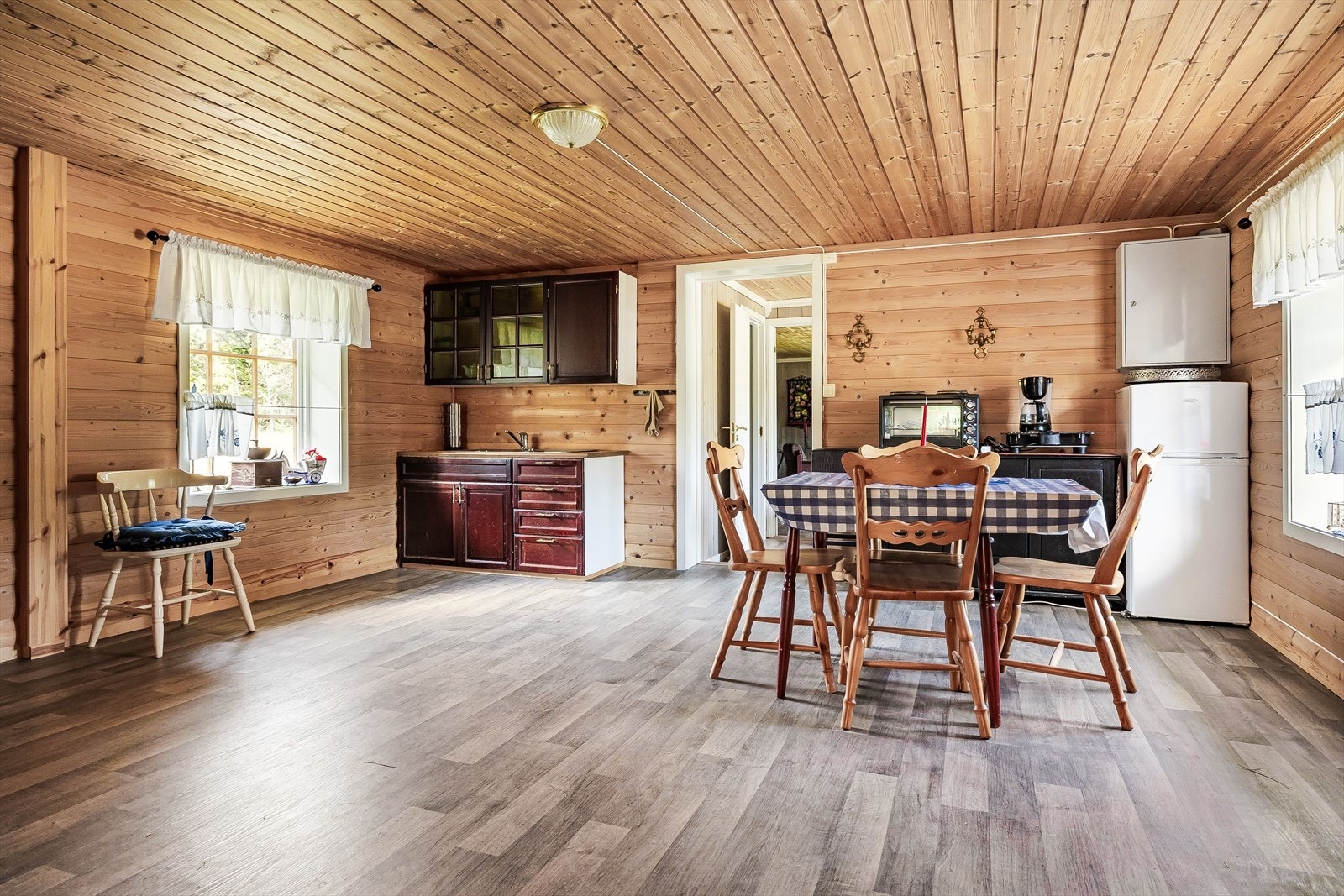 Enkel kjøkkeninnredning med over- og underskap, del med glassdører og to rustfrie kummer. Plass for frittstående kjøleskap/frys og micro. Galleribilde