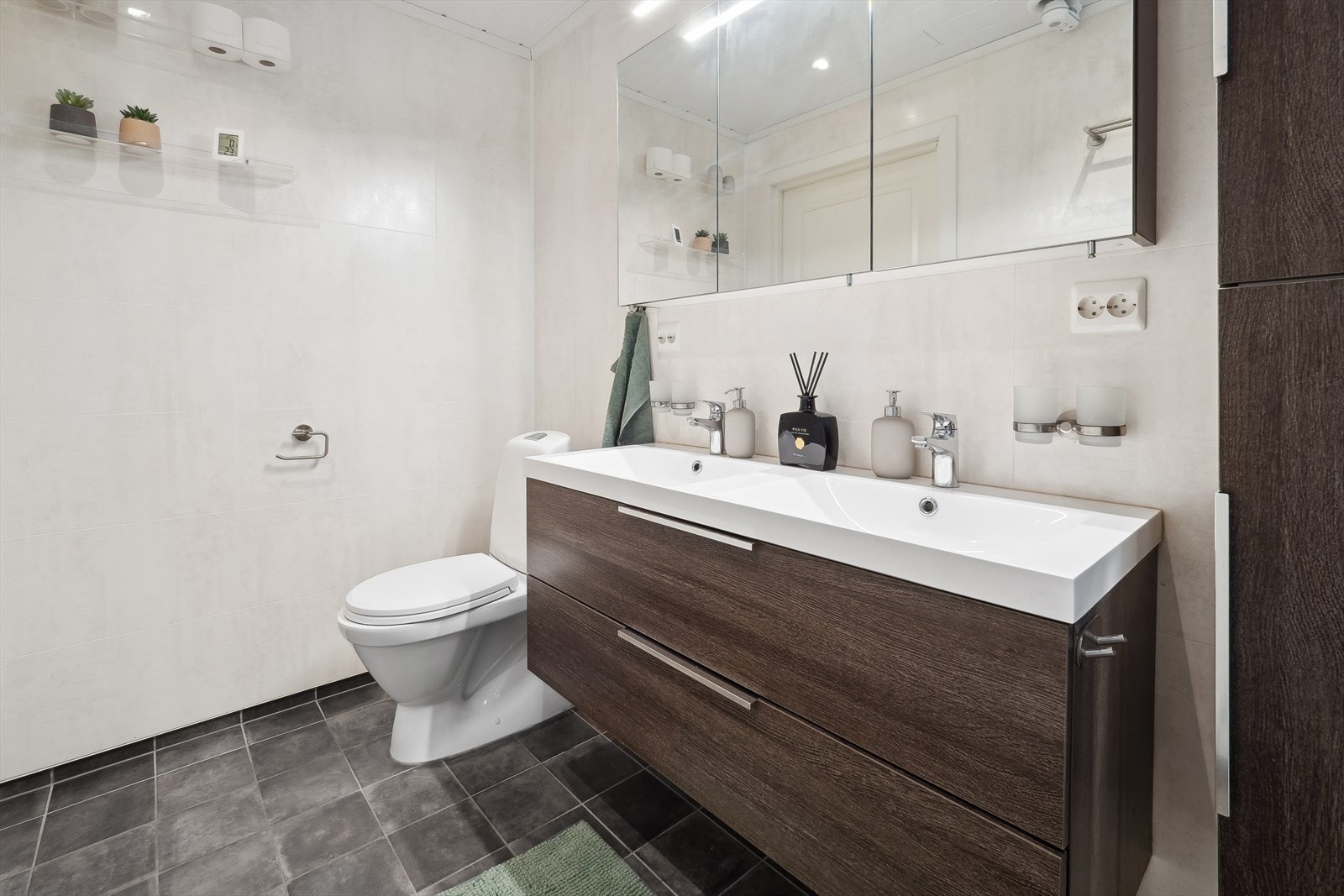 Badet har innredning med servant med skuffeseksjon, speil med tilhørende belysning, gulvstående wc og dusjkabinett. Galleribilde