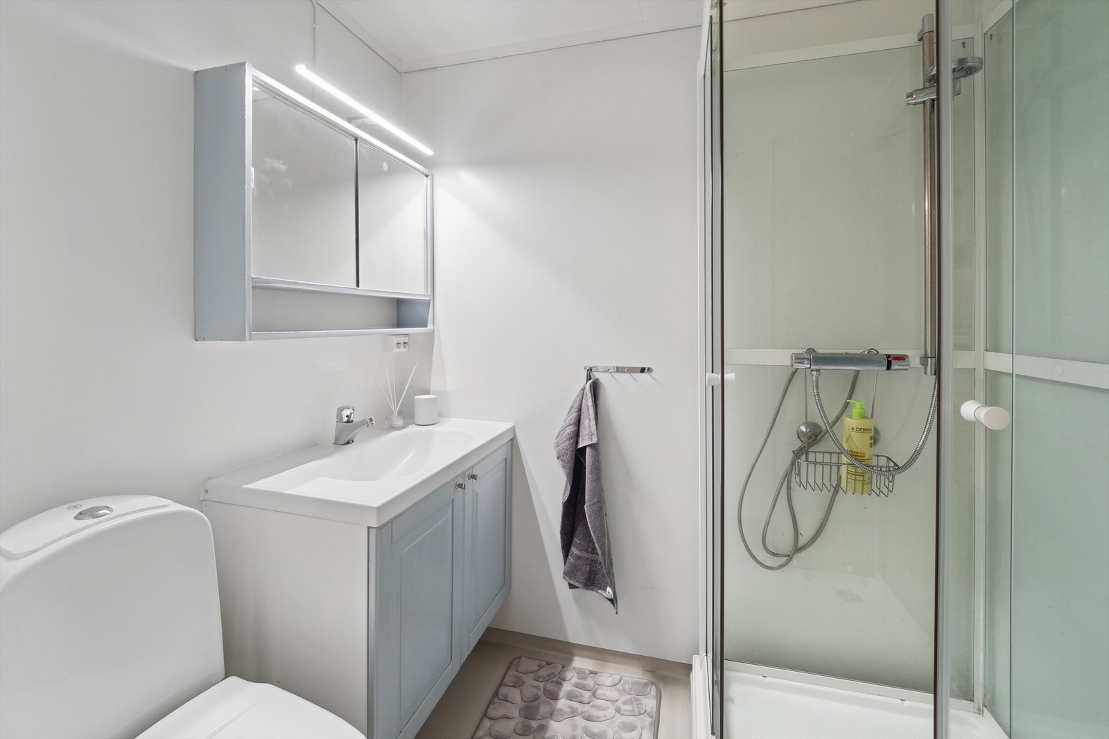 Bad i underetasje har baderomsplater på veggene og belegg på gulv med gulvvarme. Innredet med servant med underskap, speil med tilhørende belysning. Dusjkabinett og gulvmontert wc. Galleribilde