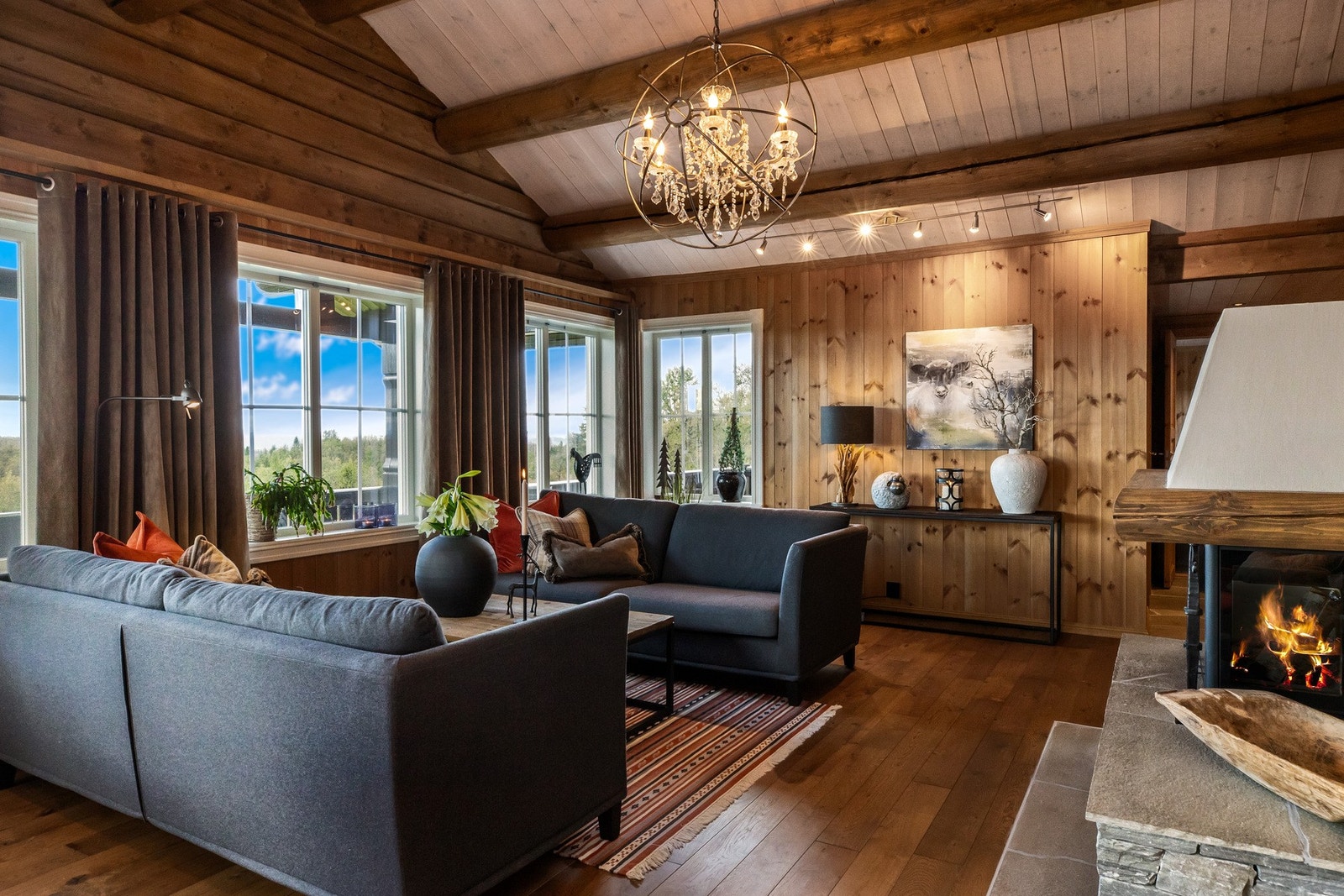 Åpen og høy himling med synlige tømmeråser, en blanding mellom tømmerdetaljer og panel på vegger som er beiset i en lun farge Galleribilde