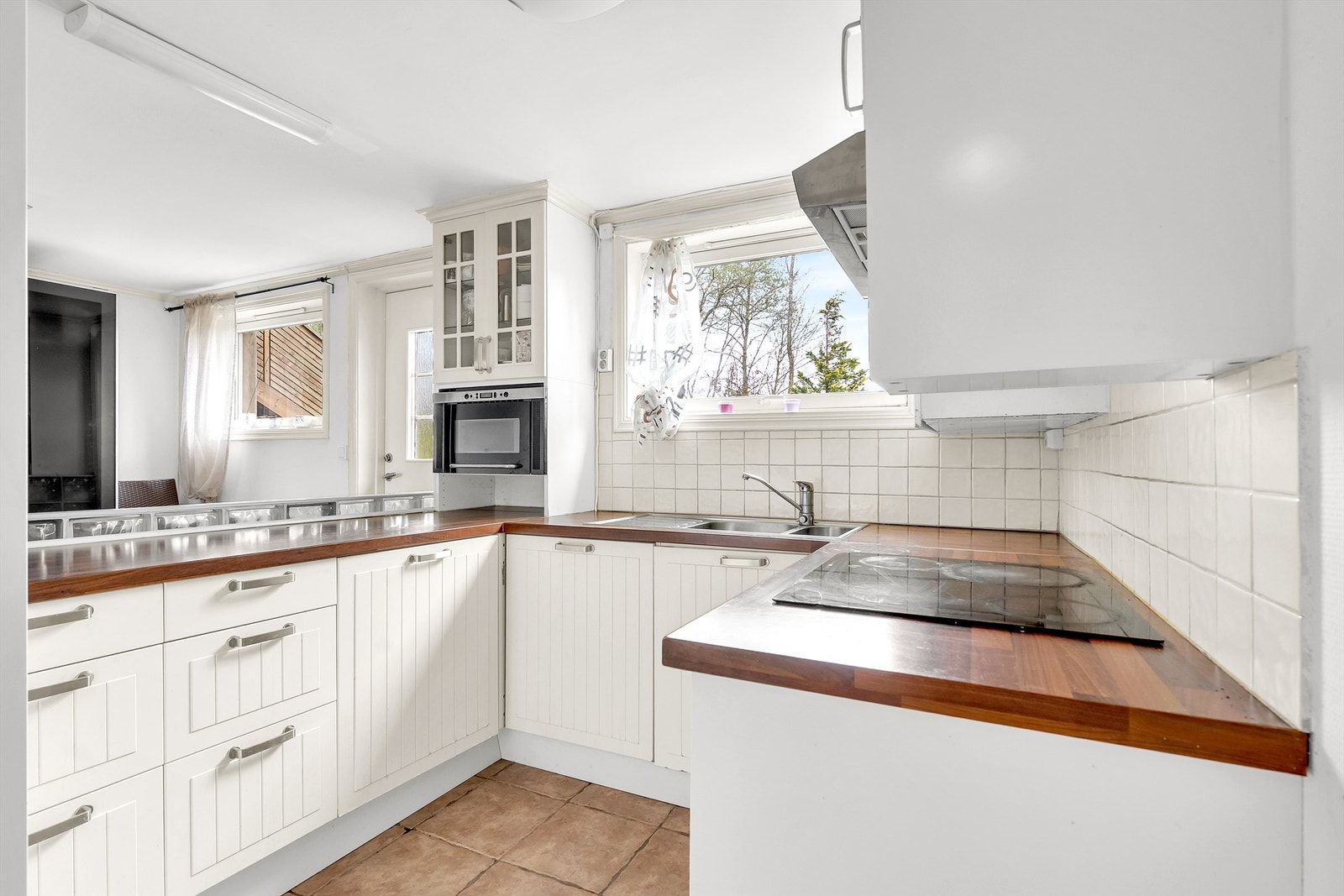 Kjøkkeninnredning med profilerte fronter, noe vitrineskap og benkeplate av laminat. Det er integrerte hvitevarer som platetopp, stekeovn, oppvaskmaskin og frittstående kjøle- og fryseskap. Galleribilde