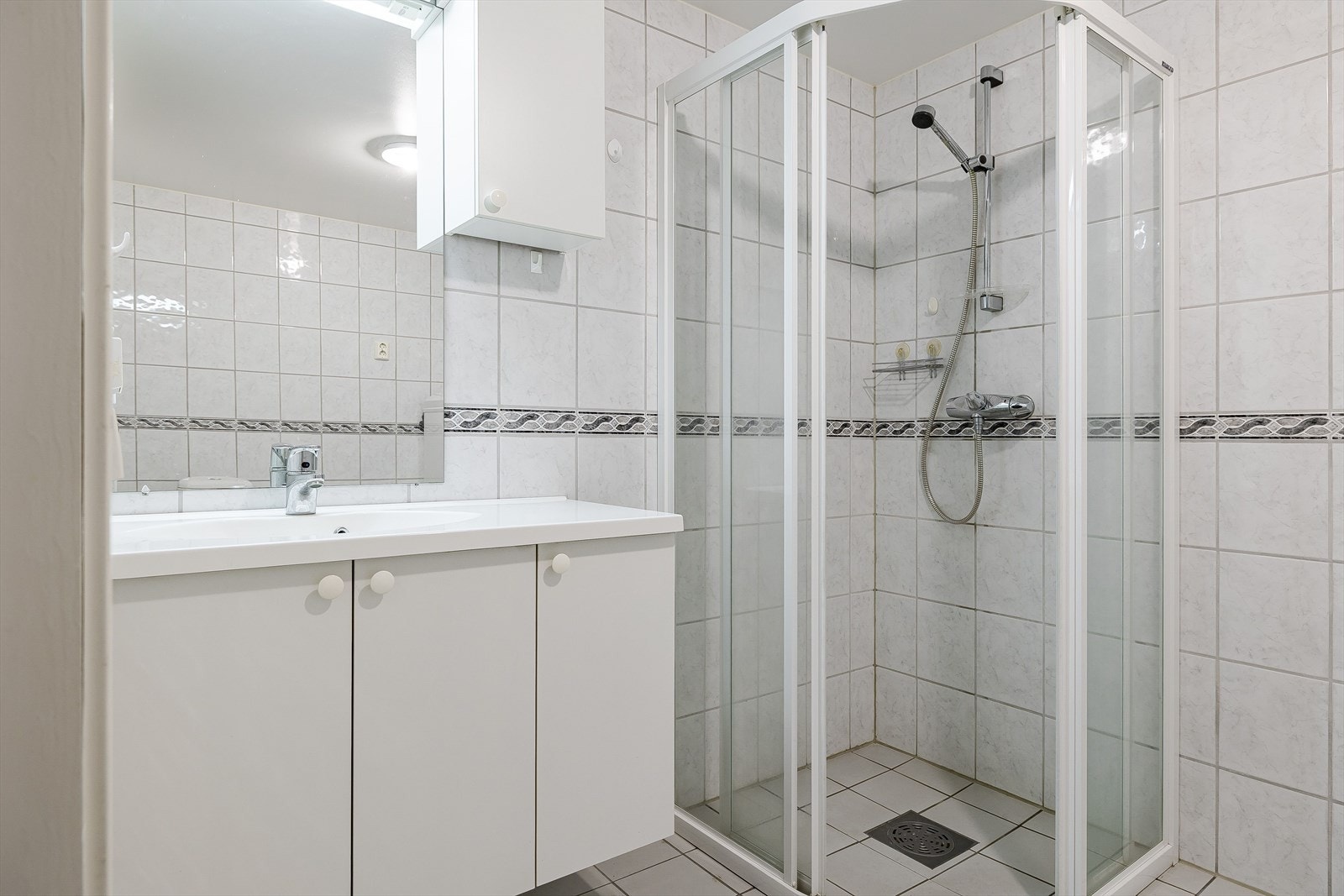 Baderommet er innredet med servant på innredning, dusjhjørne med vegghengt dusj, toalett og opplegg for vaskemaskin. Galleribilde