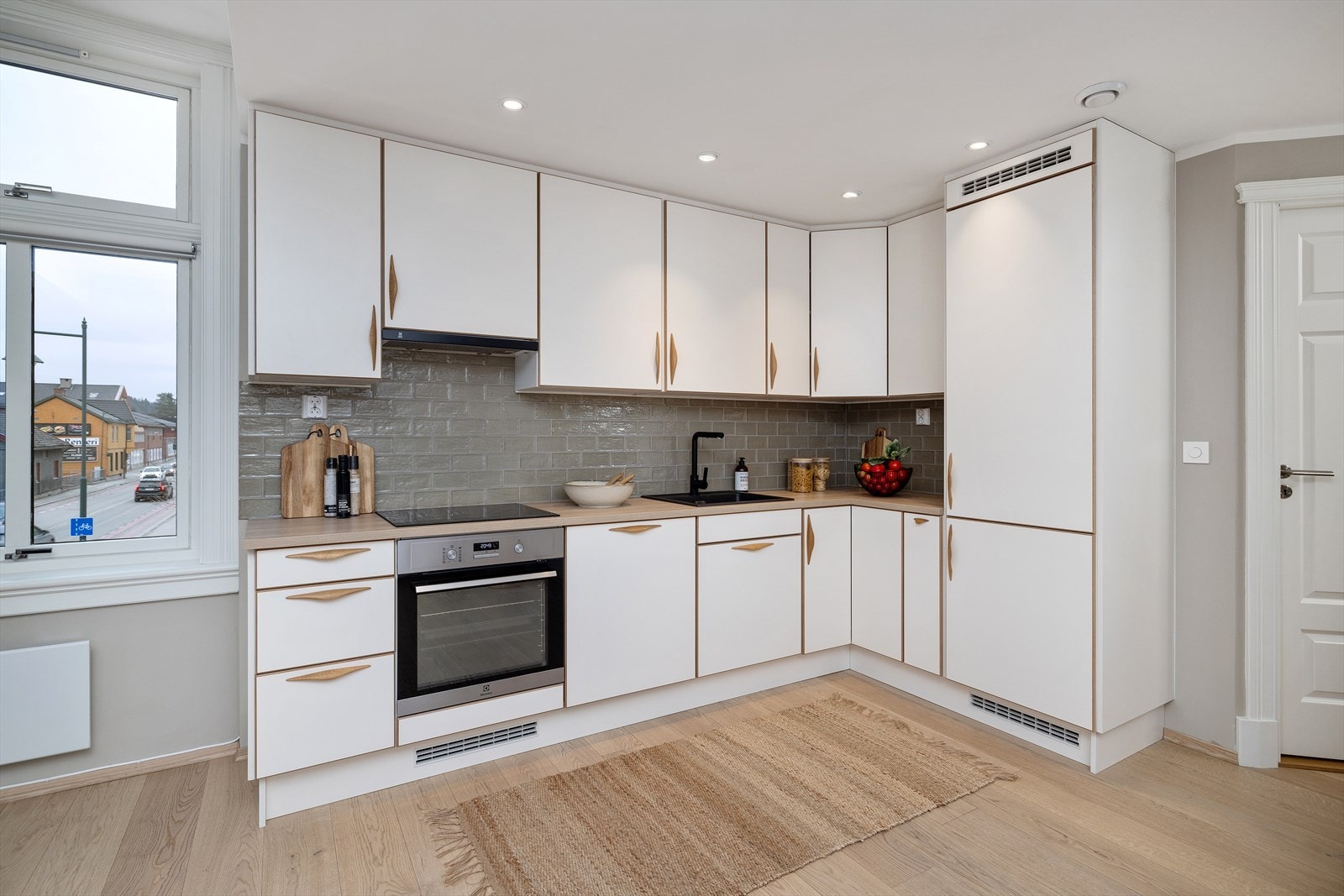 Pen kjøkkeninnredning med takhøye skap, integrerte hvitevarer, fliser over benk og downlights i tak Galleribilde