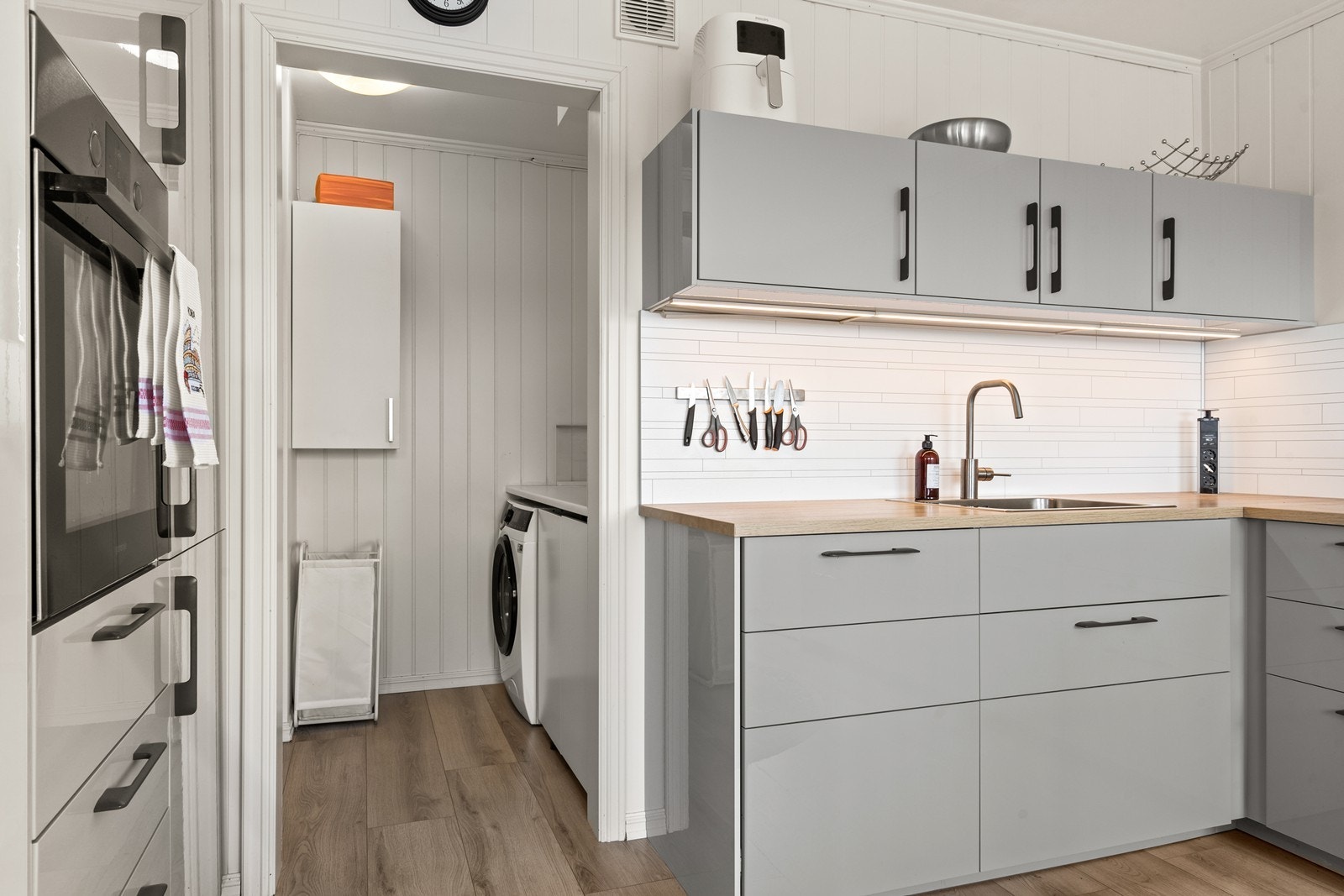 Praktisk vaskerom med skap og benkeplass på innsiden av kjøkkenet. Galleribilde