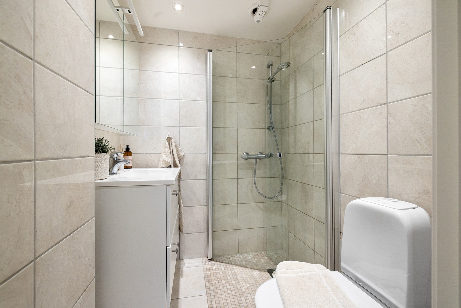 Badet har stilrene fliser på gulv og vegger. I dusjsonen er det supplert med mosaikkfliser. Galleribilde