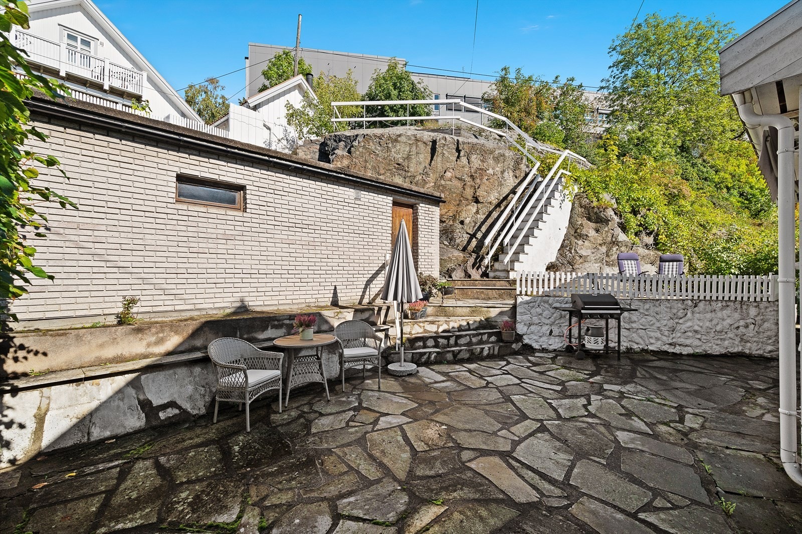 Del av tomten. Her med skiferlagt areal og trapp opp til utsiktspunktet. NB! Garasjen på bildet tilhører nabo. Galleribilde