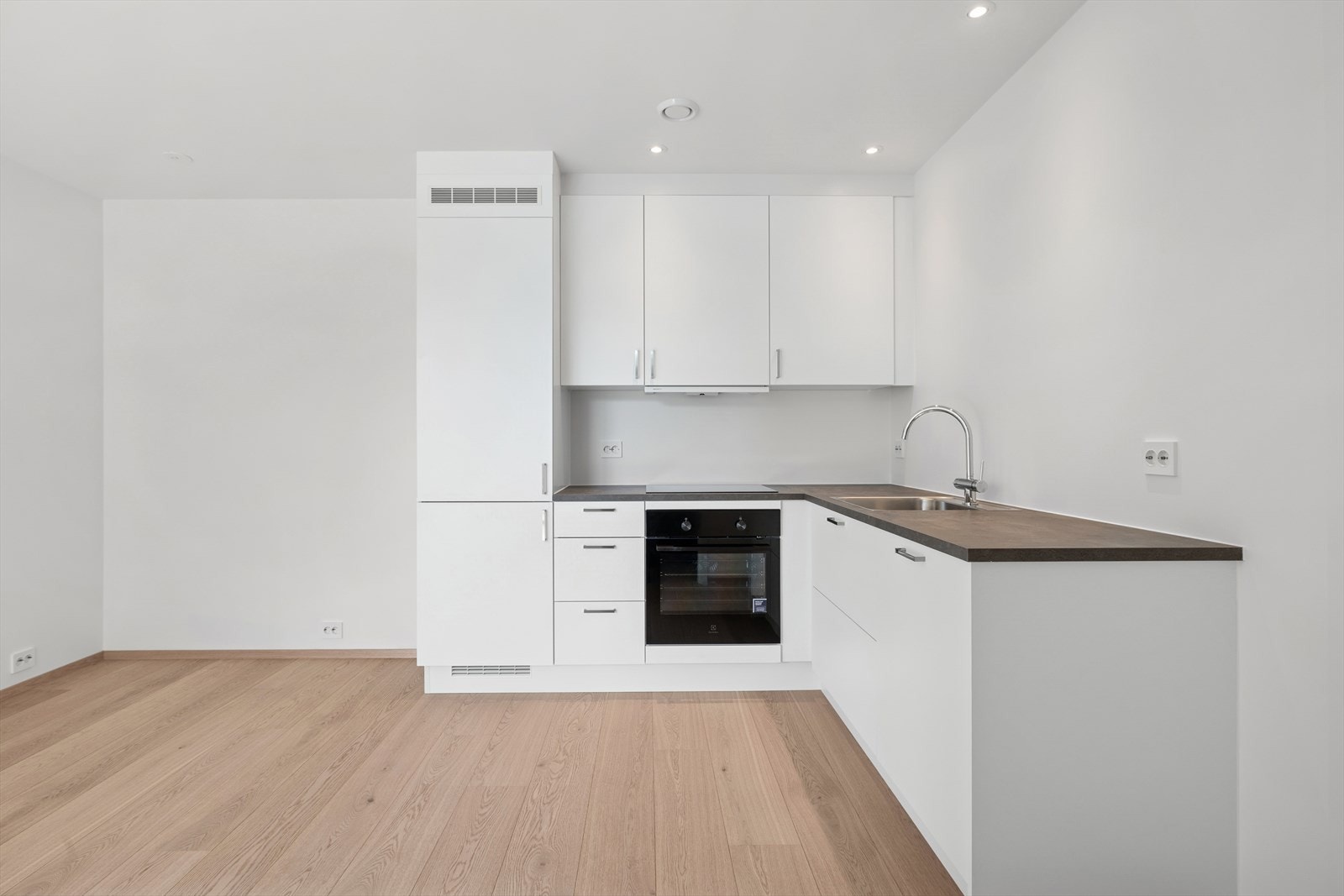 Kjøkkenet er stilrent og moderne, med innredning av hvite slette fronter og en grå benkeplate. Galleribilde