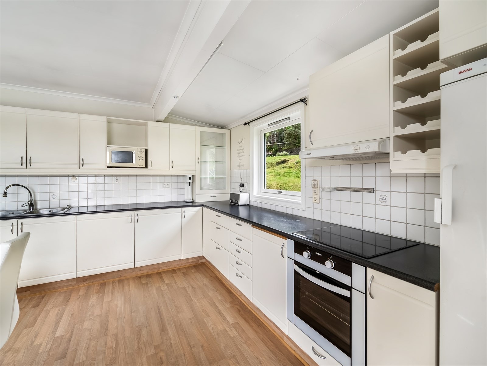 Pent kjøkken i lys utførelse med en kombinasjon av integrerte og enkeltstående hvitevarer. Galleribilde